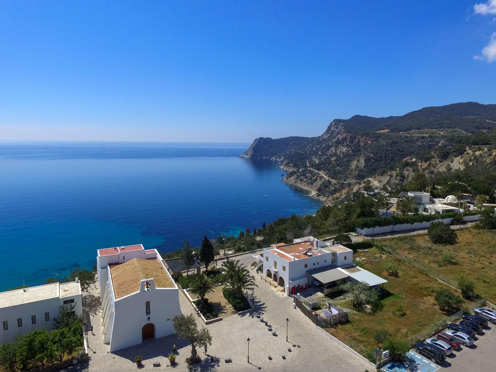 Vue en hauteur d'Es Cubells, Ibiza, avec une église blanchie à la chaux surplombant la mer bleue et le littoral accidenté